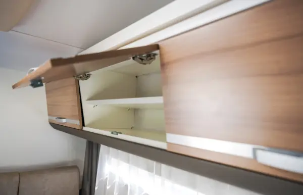 Eine Nahaufnahme auf Augenhöhe zeigt eine moderne Küchenecke mit Fokus auf der Rückwand und der Arbeitsplatte. Die Rückwand zeichnet sich durch eine warme, hellbraune Holzmaserung aus, die durch eine Reihe kleiner, eingelassener LED-Leuchten beleuchtet wird, die in die Unterseite der Oberschränke eingebaut sind. Diese Leuchten werfen ein weiches, diffuses Licht auf die strukturierte Oberfläche und schaffen so eine warme und einladende Atmosphäre.

Auf der linken Seite ist eine Edelstahlspüle mit einem eleganten, geschwungenen Wasserhahn zu sehen, die in eine helle Arbeitsplatte eingelassen ist, die ebenfalls eine Holzmaserung imitiert. Die Arbeitsplatte erstreckt sich nach rechts, wobei ihre Kante einen dunkleren Farbton aufweist, wodurch ein subtiler Kontrast entsteht.

Im Hintergrund sind dunkle Schränke mit Holzmaserung über der Küchenrückwand angebracht. Rechts neben der Spüle befindet sich eine silberne Steckdose mit drei Anschlüssen an der Küchenrückwand. Weiter rechts ist eine weitere Steckdose mit zwei Anschlüssen zu sehen. Die Unterschränke, die links und unten im Bild teilweise zu sehen sind, haben ebenfalls eine dunkle Holzmaserung und minimalistische schwarze Griffe. Der Gesamteindruck ist der eines sauberen, modernen und gut beleuchteten Küchenbereichs.